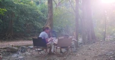 Anne ve oğlunun kampta nehrin kenarında otururken çekilmiş kamera görüntüleri.