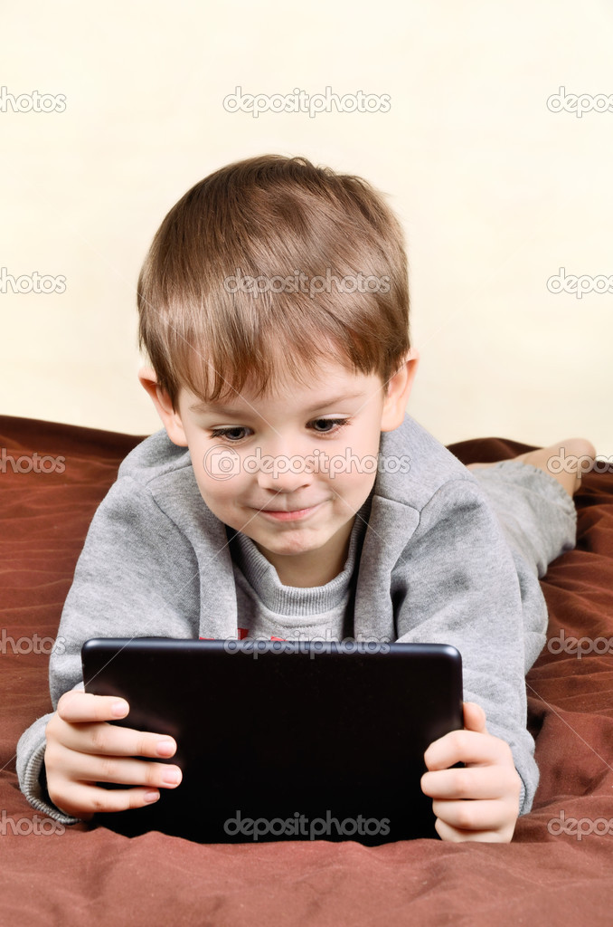 smiling boy is lying and playing on a tablet