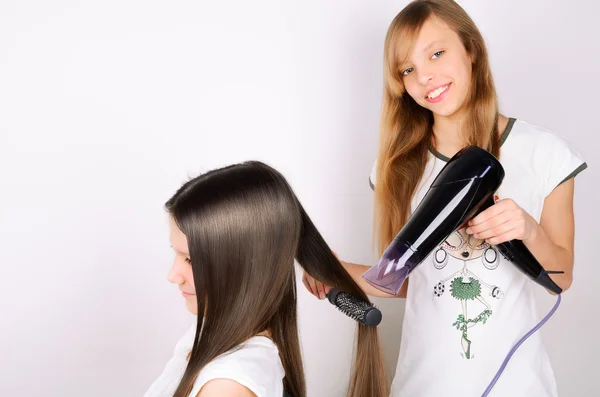 Chica seca el cabello el secador de pelo otra chica adolescente —  Fotos de Stock