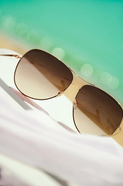 Sunglasses and white chiffon pareo on background of sea and sand — Stock Photo, Image