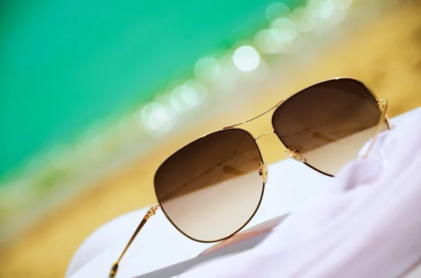 Sunglasses and white chiffon pareo on background of sea and sand — Stock Photo, Image