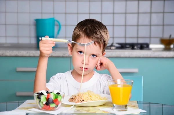 Sad little boy sits at the dining table and looking spaghetti — Stock Photo, Image