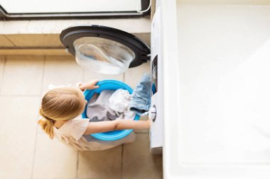 Yedi yaşında beyaz bir kız, ev işlerine yardım ediyor. Kid 'in evde çamaşır makinesinden giysilerini çıkarırken çekilmiş bir portresi.