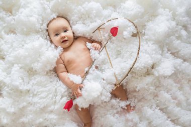 Beyaz bulutların üzerinde beyaz arkaplan ve kalp okuyla gülümseyen beyaz bir bebek. Sevgililer günün kutlu olsun..