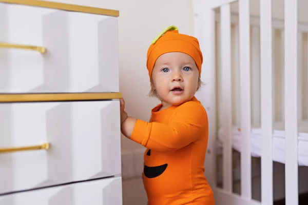 Χαριτωμένο καυκάσιο μωρό κοριτσάκι ενός έτους σε πορτοκαλί κοστούμι με πρόσωπο κολοκύθας στο σπίτι. Καλή ιδέα Απόκριες — Φωτογραφία Αρχείου