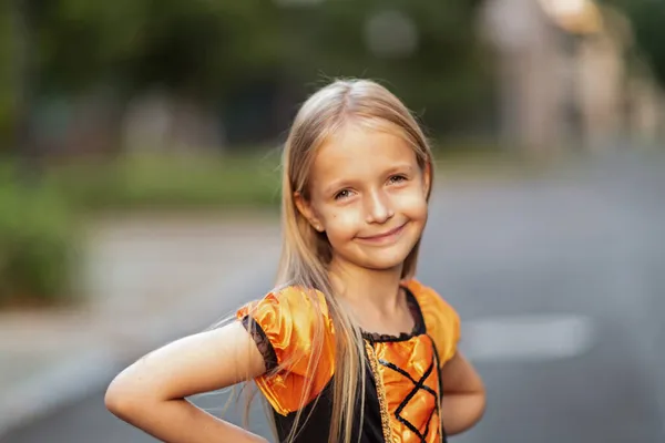 Lifestyle portrait of Happy Little caucasian Girl with blonde hair seven years old in black orange costume of which celebrating Halloween alone outdoor during Coronavirus covid-19 pandemic quarantine. — Stock Photo, Image