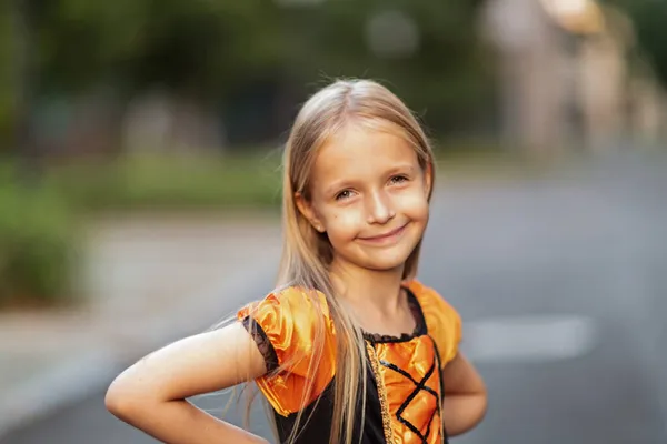 Stile di vita ritratto di Happy Little caucasico Ragazza con i capelli biondi di sette anni in costume arancione nero di cui festeggia Halloween da solo all'aperto durante la quarantena pandemica Coronavirus covid-19. — Foto Stock