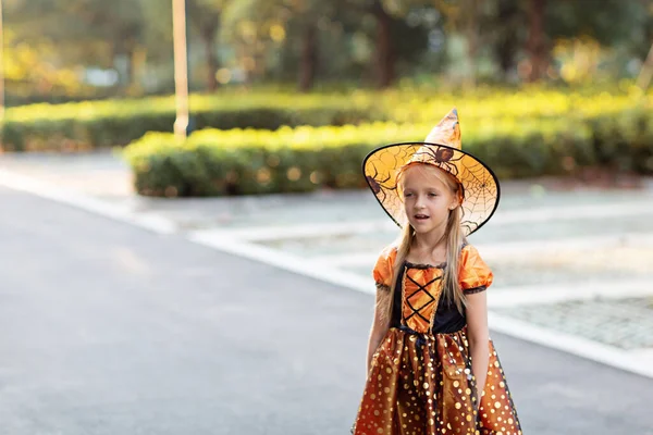 Portret życia Happy Little kaukaska dziewczyna z blond włosami siedem lat w czarnym pomarańczowym stroju, z których świętuje Halloween sam na świeżym powietrzu podczas Coronavirus covid-19 pandemia kwarantanny. — Zdjęcie stockowe