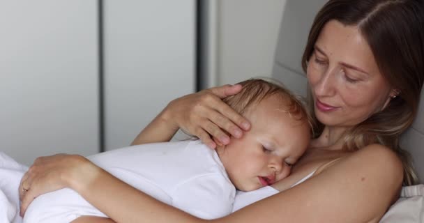 Joven hermosa madre abraza hija bebé que duerme en ella en casa. Feliz familia mamá y lindo niño hijo disfrutando de momentos dulces juntos. Movimiento lento — Vídeo de stock