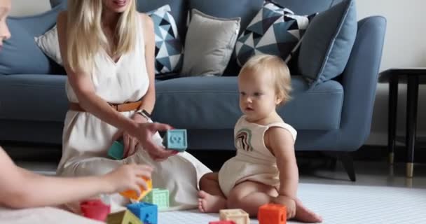 Young caucasian mother or nanny playing with cute baby one year old and elder daughter, learning to build a tower from cubes for kids. Three generation family spending time together and enjoying life — Stock Video