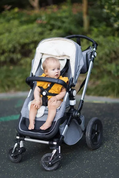 Een lief blank meisje van tien maanden in een kinderwagen buiten. Klein kind in kinderwagen. Het kleine kind zit in een kinderwagen. Zomer wandelingen met kinderen. Familie vrijetijdsbesteding met klein kind. — Stockfoto