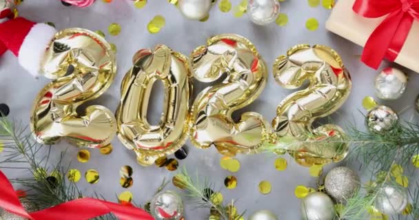 Felice anno nuovo 2022 sfondo. Palloncini metallici color oro su cemento grigio con coriandoli. Posa piatta, vista dall'alto, mockup, sopraelevata. Festa delle vacanze invernali. Rallentatore — Video Stock