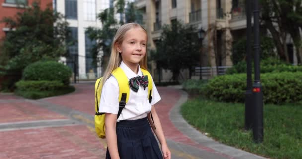 Gelukkige kleine blanke blonde meisje zeven jaar oud in uniform met gele rugzak terug naar school na de zomervakantie of Coronavirus covid-19 quarantaine. 4k slow motion — Stockvideo