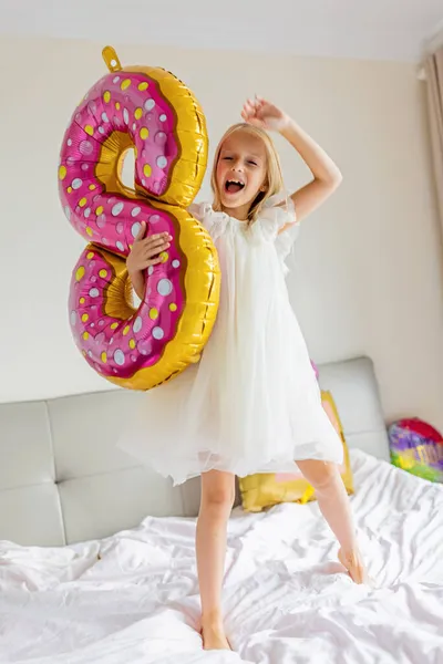 Beltéri lövés elég vidám aranyos aranyos aranyos aranyos lány gyerek ünnepli nyolc éves születésnapját fényes és színes lufik feliratos szavak maradnak mesés, visel alkalmi divatos ruha — Stock Fotó