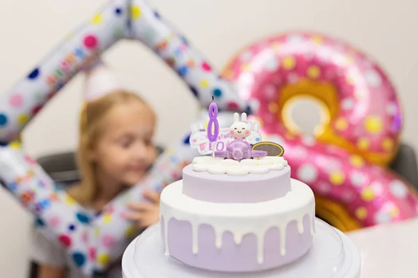 Boldog kis kaukázusi lány pozitív érzelmekkel az arcán, aki 8 éves születésnapját ünnepli otthon. Őszinte életmód portré Kölyökről, amint gyertyákat fúj a tortára. Nappali fóliával díszítve — Stock Fotó