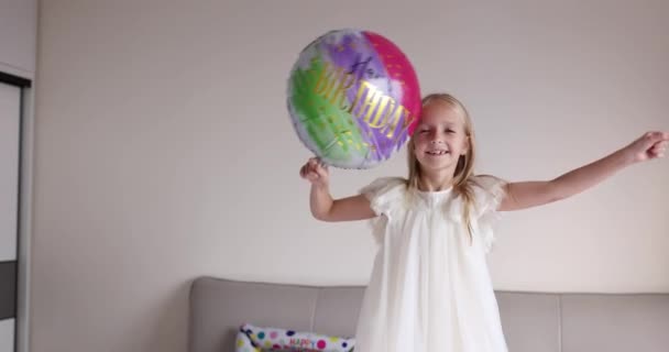 Beltéri felvétel elég vidám aranyos aranyos aranyos lány gyerek ünnepli nyolc éves születésnapját fényes és színes lufik, visel alkalmi divatos ruhát. A kölyök jól érzi magát. Lassú mozgás. — Stock videók