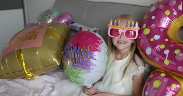 Indoor shot van mooie vrolijke schattige schattige meisje kind vieren acht jaar oude verjaardag met heldere en kleurrijke ballonnen, het dragen van casual modieuze jurk. Dat joch heeft plezier. Langzame beweging — Stockvideo