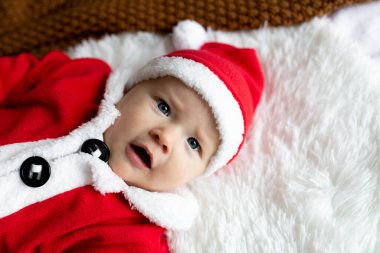 Yeni doğan bebeğin yakın plan portresi. 4-5 aylık Noel Baba kostümüyle yatakta örülmüş battaniyeye uzanmış tatlı beyaz bir bebek. Mutlu Noeller ve mutlu yıllar 2022
