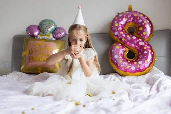 Indoor shot of pretty joyful cute adorable girl kid celebrando el cumpleaños de ocho años con globos brillantes y coloridos con palabras de inscripción permanecen fabulosas, vistiendo vestido casual de moda —  Fotos de Stock