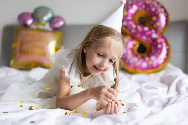 Kapalı mekanda, üzerinde yazılar olan parlak ve renkli balonlarla sekiz yaşındaki bir kızın doğum gününü kutlayan sevimli, sevimli bir kız çocuğu. — Stok fotoğraf