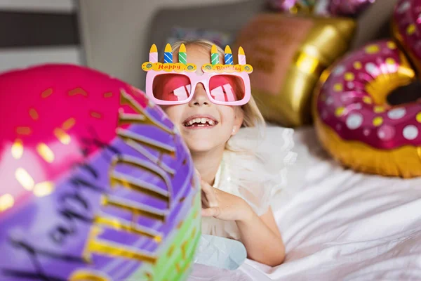 Внутренний снимок довольно радостный милый очаровательный ребенок девушка празднует восьмилетний день рождения с яркими и красочными воздушными шарами с надписью слова остаются сказочными, носить повседневную модную одежду — стоковое фото