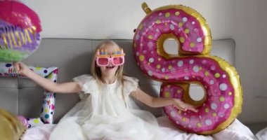 Hoş, sevimli, sevimli bir kızın, sekiz yaşındaki doğum gününü parlak ve renkli balonlarla kutladığı, günlük moda elbiseler giydiği bir fotoğraf. Çocuk eğleniyor. Yavaş çekim
