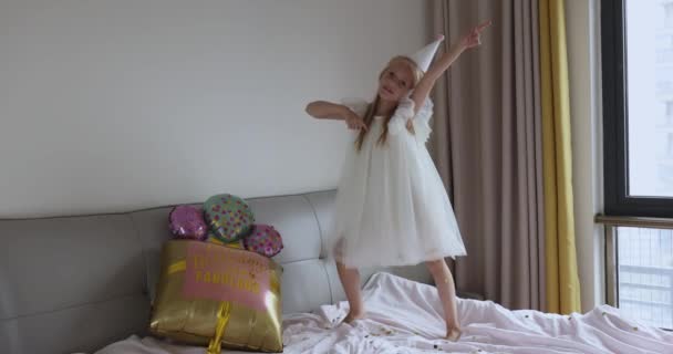 밝고 화려 한 풍선을 끼고 평범 한 드레스를 입고 8 살 생일을 축하하는 예쁘고 귀여운 여자 아이가 문 앞에서 찍은 사진입니다. 재밌게 놀고 있어. 느린 동작 — 비디오