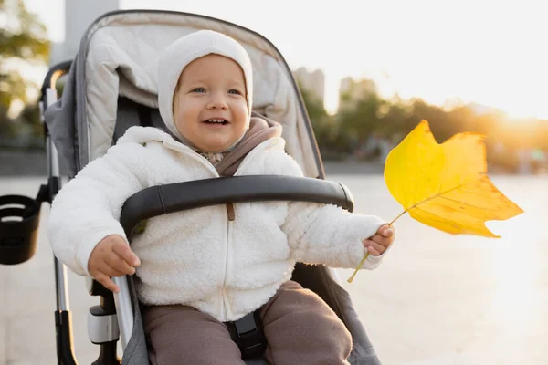 Симпатичная годовалая девочка держала упавший желтый лист во время осенней прогулки на свежем воздухе. Счастливый здоровый малыш с красивым лицом, радующийся жизни и осеннему сезону на закате — стоковое фото