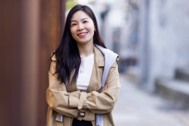 Güzel iş kadını esmer saçlı Asyalı kadın sonbaharda açık havada sıradan bir trençkot giyiyor.