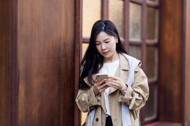 Sosyal medyada fotoğraf paylaşırken cep telefonu ekranına bakıp ilginç içerik metinleri hakkında düşünen sıradan giyinmiş Asyalı şık genç bir kadın. Yaşam stili blogcusu kontrol ediyor