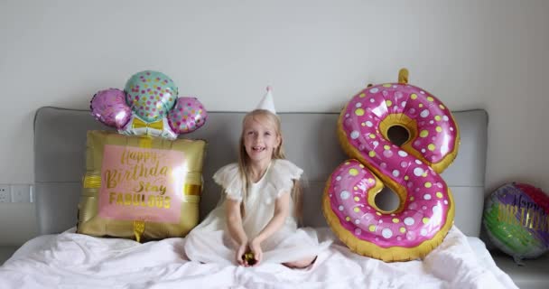 Критий знімок досить радісної милої чарівної дівчинки, яка святкує восьмирічний день народження з яскравими і барвистими повітряними кулями, в повсякденній модній сукні. Малюк розважається. Повільний рух — стокове відео
