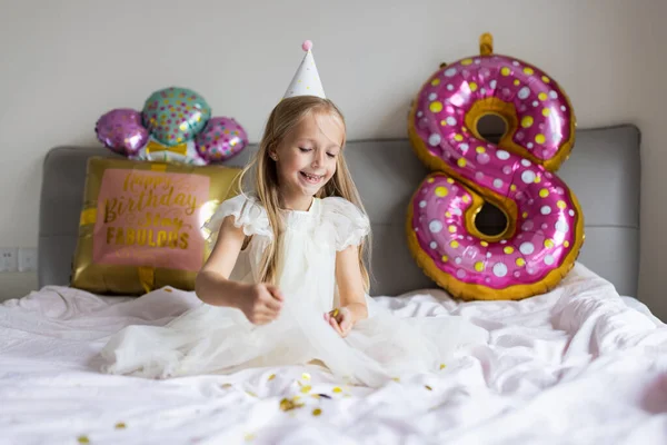 Vnitřní záběr docela radostné roztomilé roztomilé holčičky oslavující osm let staré narozeniny s jasnými a barevnými balónky s nápisem slova zůstat báječný, na sobě ležérní módní šaty — Stock fotografie