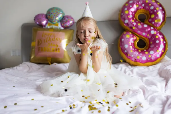 Indoor shot of pretty joyful cute adorable girl kid celebrando el cumpleaños de ocho años con globos brillantes y coloridos con palabras de inscripción permanecen fabulosas, vistiendo vestido casual de moda —  Fotos de Stock