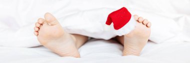 Başparmağında kırmızı Noel Baba şapkası olan çocuk ayakları. Fotokopi alanı ile çıplak ayaklı Noel konsepti. Mutlu yıllar 2022 ve Xmas tatil rahatlama konsepti. Web tasarımı için yatay uzun pankart