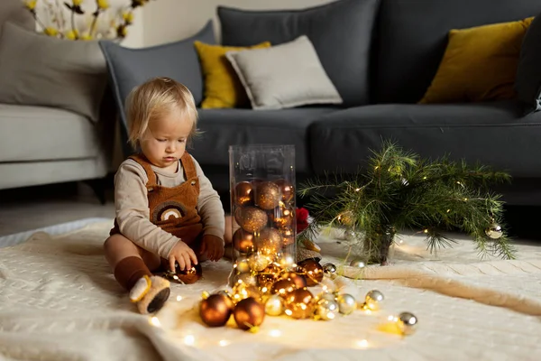 Retrato de estilo de vida del lindo bebé caucásico de un año jugando con adornos en el suelo en casa. Feliz Navidad y feliz año nuevo 2022 —  Fotos de Stock