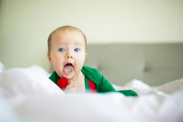 Cute dziewczynka kaukaska sześć miesięcy w kostiumie elfa zielony kolor. Uroczy pomocnik Santa leżący na łóżku w domu na białym tle — Zdjęcie stockowe