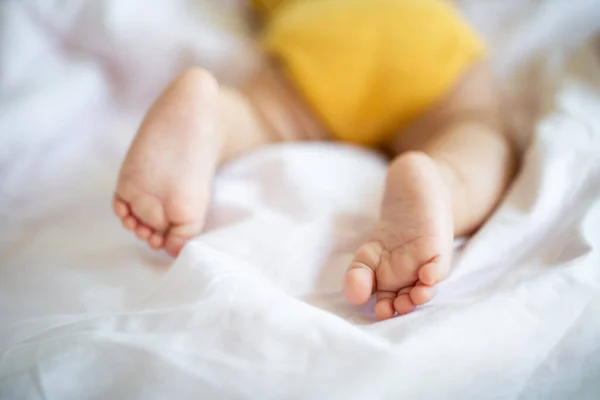 Voeten van een blanke blonde baby van zeven maanden oud die thuis op bed ligt. Kind draagt leuke kleding trendy kleuren: verhelderend geel. Slapen voor zuigelingen — Stockfoto
