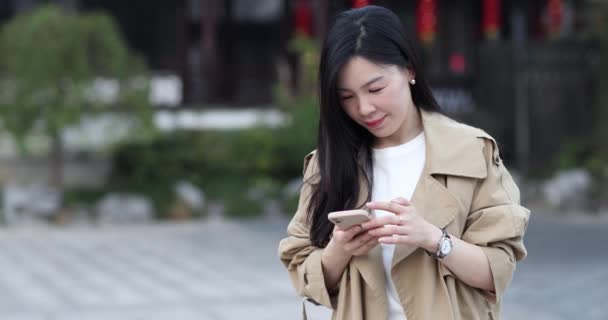 Portret profesjonalnej biznesmenki korzystającej ze smartfona, przeglądającej online, czytającej wiadomości na telefonie komórkowym w mieście. Młody azjatycki influencer z uśmiechniętą twarzą za pomocą mediów społecznościowych odkryty w — Wideo stockowe