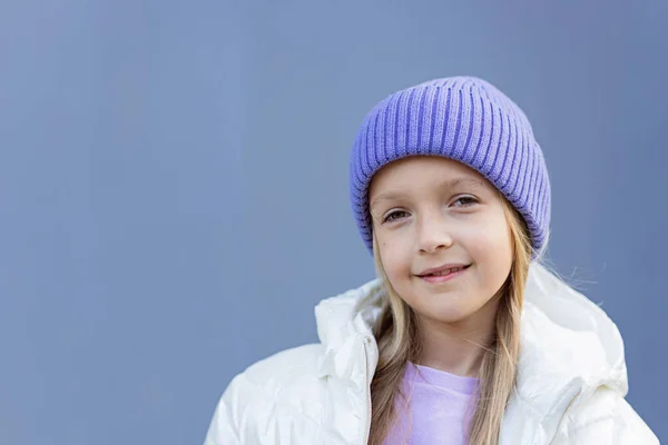 Милая маленькая белая девочка восьми лет с светлыми волосами, улыбающаяся на улице. Парень в стильной рубашке и вязаной шляпе фиолетового цвета. Модный цвет 2022 года очень peri — стоковое фото