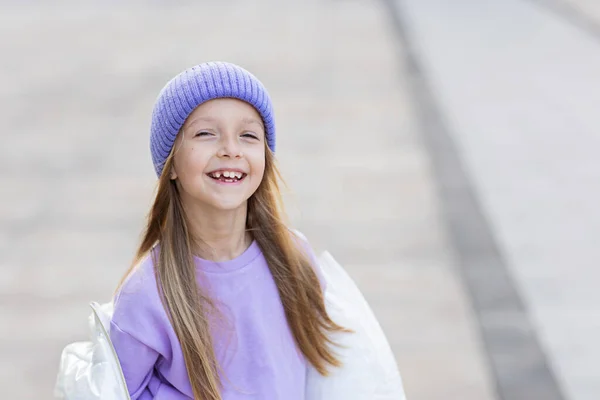 Słodka, mała, biała dziewczynka, 8 lat, z blond włosami, uśmiechnięta na zewnątrz. Dziecko w stylowej koszuli i dzianiny fioletowy kolor kapelusza. Modny kolor 2022 roku bardzo peri — Zdjęcie stockowe