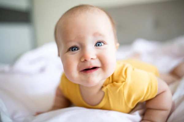 Bebê loiro caucasiano de sete meses deitado na cama em casa. Kid vestindo roupas bonitos cores da moda: iluminando amarelo. Infantil brincando com brinquedos — Fotografia de Stock