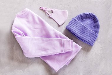 Gri beton zeminde düz örülmüş şapka ve koruyucu yüz maskesi. 2022 yılının rengi çok peri. Renk konsepti, kopyalama alanı ile modelleme