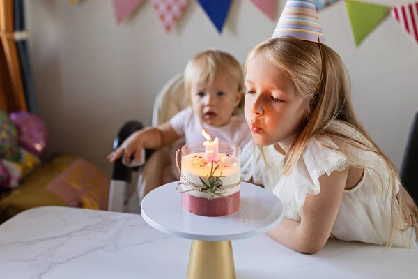 Birthday party at home. Happy little caucasian girl and cute baby with positive emotion on face celebrating first birthday at home. Candid lifestyle portrait of Kid blowing candles on cake. Living — Stockfoto