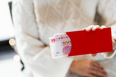 Çin Yeni Yıl kutlamaları konsepti. Genç Asyalı kadın, Bahar Festivali için 100 Yuan nakit parayla el ele tutuşuyor..