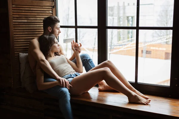 Porträt eines charmanten jungen Paares zu Hause. Mann umarmt seine Freundin am Fenster. Zwei Menschen entspannen zusammen — Stockfoto