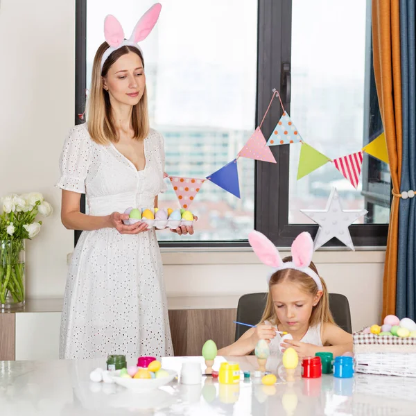 Bonita madre e hija con orejas de conejo y pintando huevos de Pascua en casa durante el brote de coronavirus covid-19. — Foto de Stock