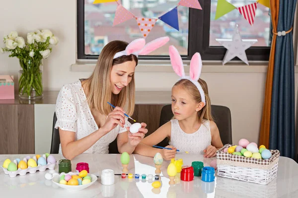 Bonita madre e hija con orejas de conejo y pintando huevos de Pascua en casa durante el brote de coronavirus covid-19. — Foto de Stock