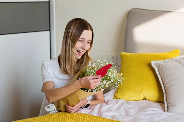 Bella giovane donna caucasica che tiene mazzo di fiori in camera da letto. Buon San Valentino. rapporto lontano e concetto di amore — Foto Stock