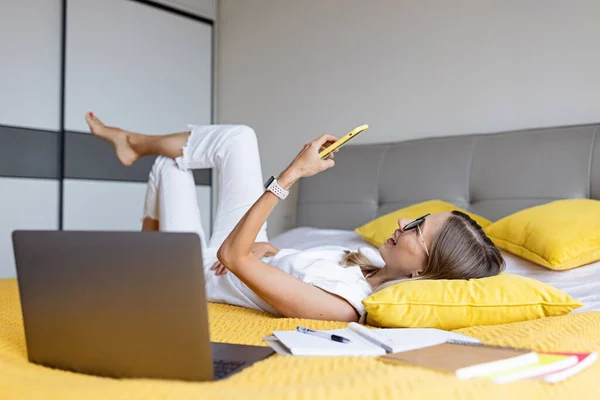 Young Woman student studying online via video chat. Stylish freelancer works from home. Blogger working from home office. Millennial business woman lying on bed in modern apartment. - Stok İmaj
