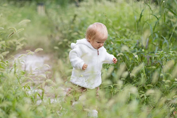 Портрет милой маленькой кавказской девочки в возрасте одного года делает первые шаги и учится ходить в парке осенью. Стильный младенец с светлыми волосами и голубыми глазами в модной одежде. Счастливый — стоковое фото